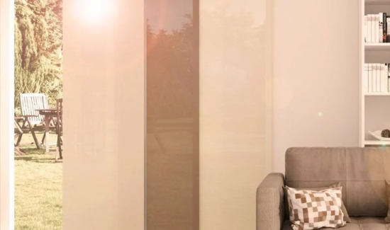 Cremefarbiger Flächenvorhang an einem hohen Fenster hinter einem hellbraunen Sofa