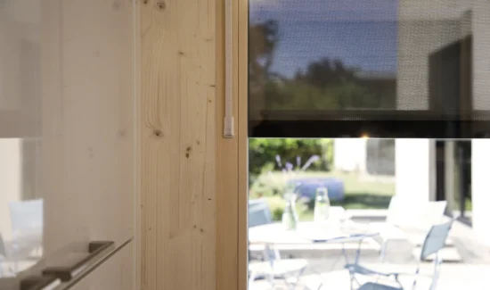 Moderner Innenraum mit Blick auf einen sonnigen Garten durch ein Fenster mit einem halb heruntergelassenen Rollladen.